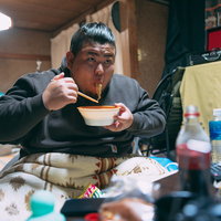 自宅の汚部屋でラーメンを啜る無精髭の男性の写真