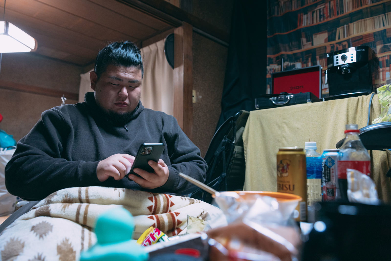 スマホを操作する肥満男性がいる部屋で食事をしている様子［モデル：ノリックス］