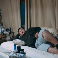 汚部屋で肘枕をして横たわる肥満体の男性の写真