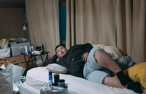 汚部屋で肘枕をして横たわる肥満体の男性