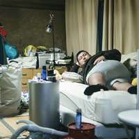 散らかった部屋で肘枕をして寝転がるデブ男性の写真