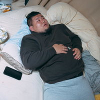 食いすぎてベッドで横になる男性、散らばるお菓子の袋の写真