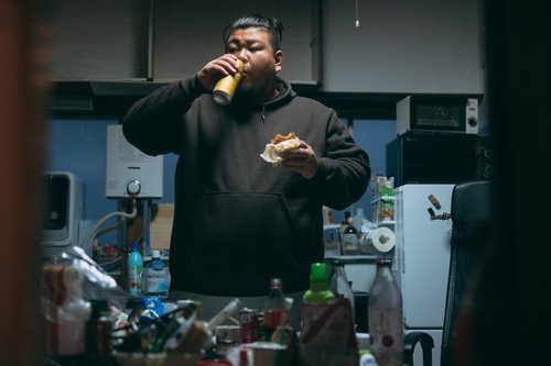 散らかったキッチンで立ち飲みする男性の写真