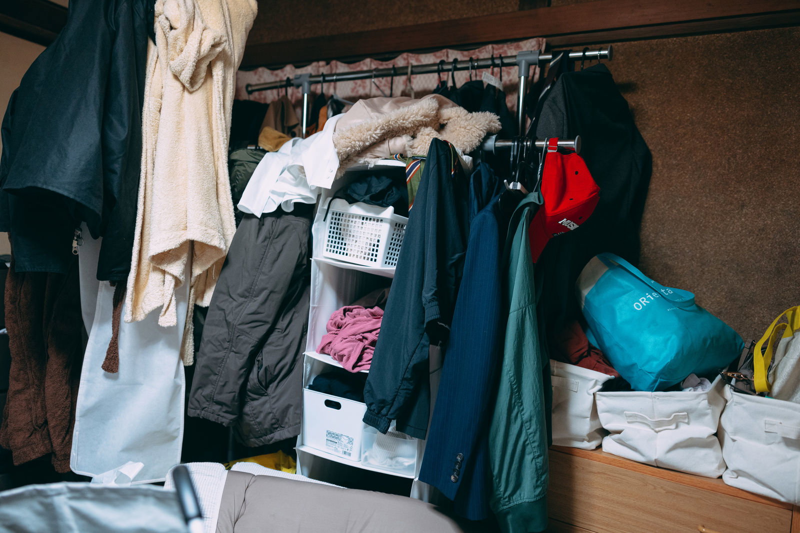 衣類が詰め込まれたハンガーラックと床に散らかった衣服や荷物