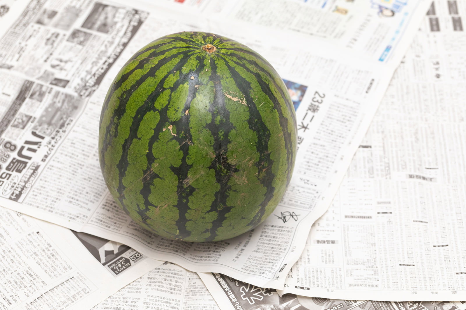 新聞紙の上に置いた丸ごと一玉のスイカ