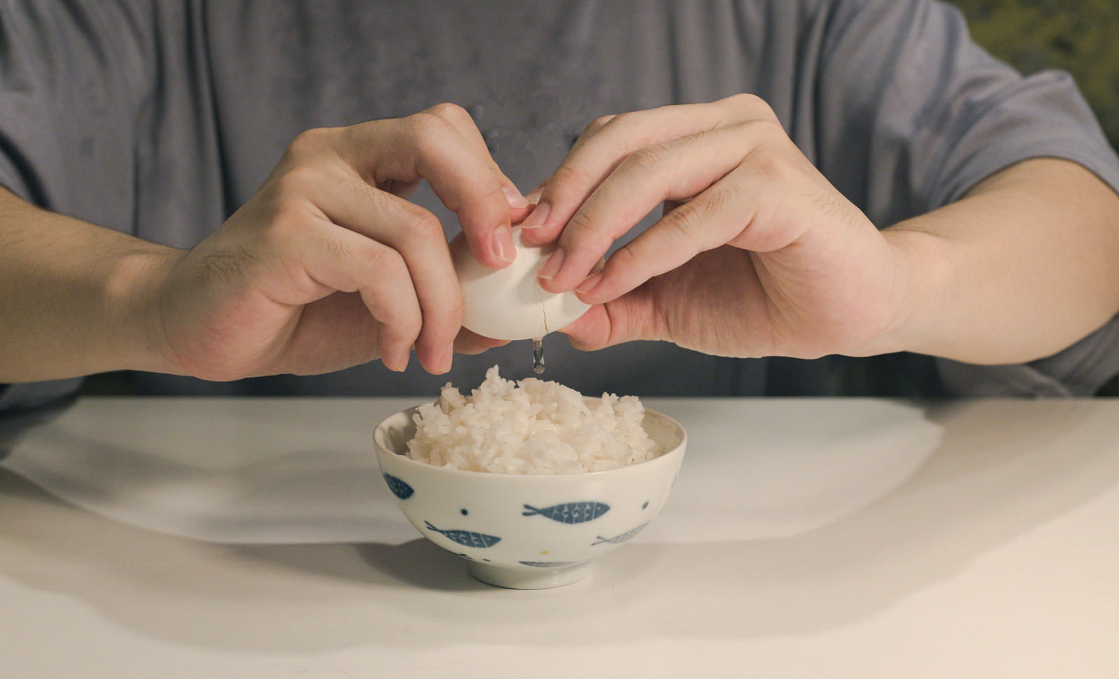 白いご飯の入った茶碗の上で卵を割ろうとしている手元