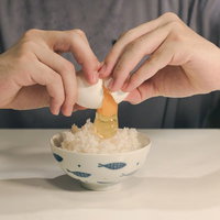 白い茶碗に生卵を割き入れる卵かけご飯の調理風景の写真