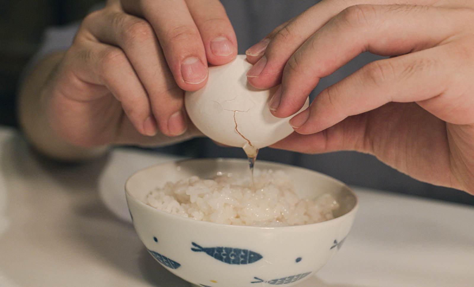白い茶碗のご飯の上で卵を割ろうとする両手