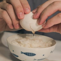 卵の殻を割って白いご飯に落とす手元の調理風景の写真
