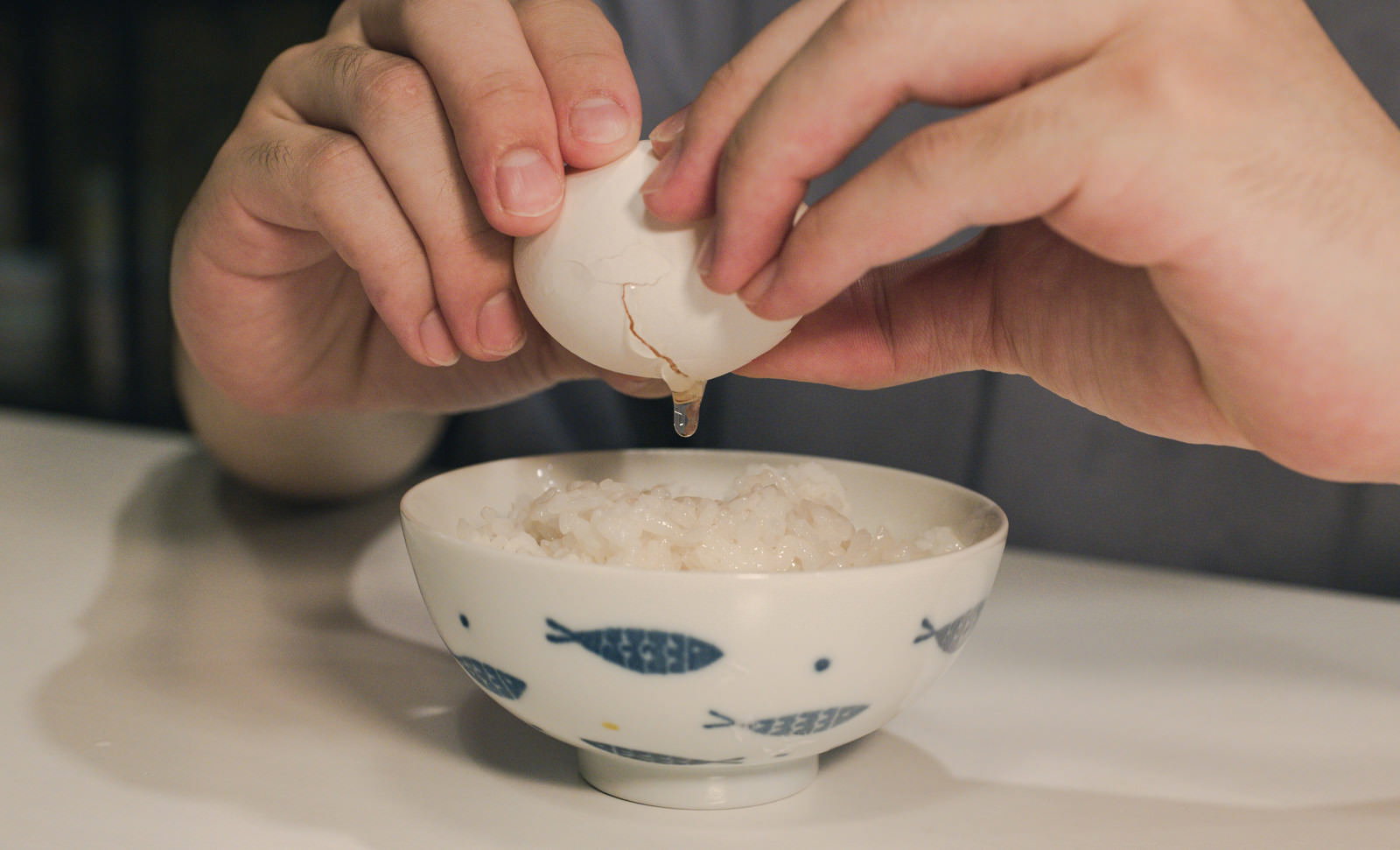 白い茶碗に盛られた白米に生卵を落とし、手で卵の殻を持つ卵かけご飯