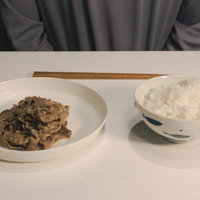 白い皿に盛られた牛肉の煮物と茶碗のご飯の写真