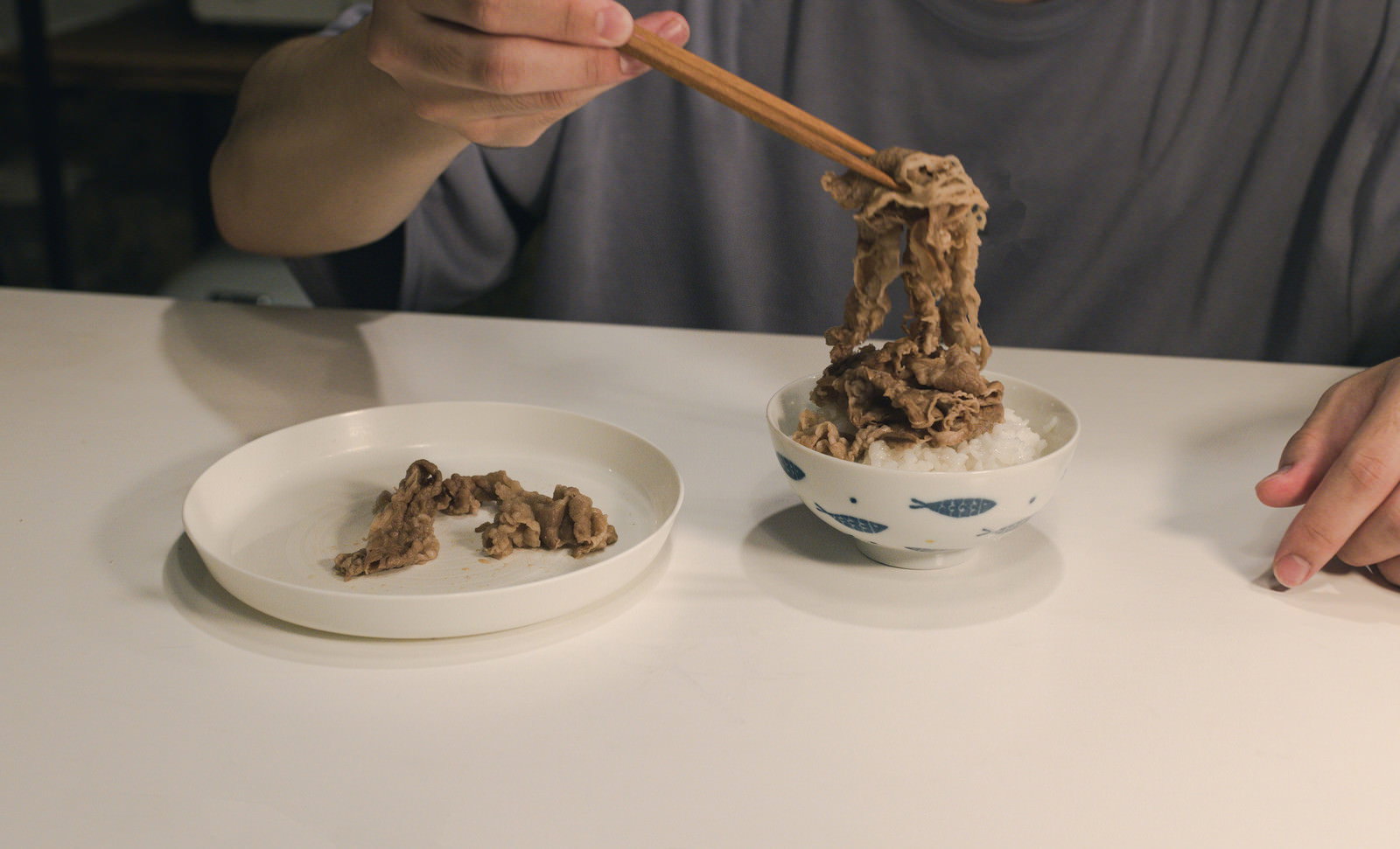 箸で牛肉を持ち上げている食事の様子、白米の入った茶碗と牛肉料理の皿