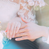 ピンクのブーケを持つ結婚指輪をはめる新郎新婦の手の写真