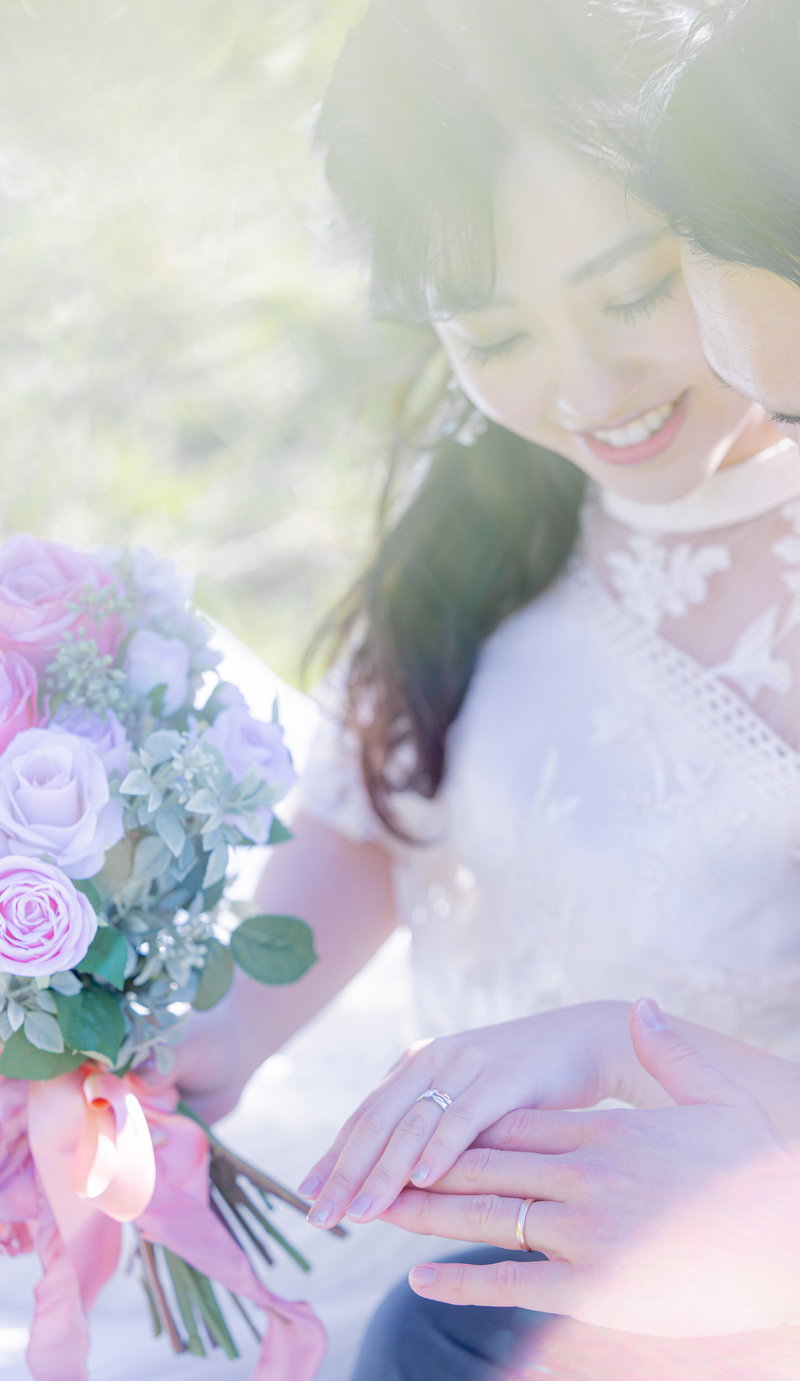 ピンク色と紫の薔薇のブーケを持ち、結婚指輪を確認する新婦と新郎［モデル：河村友歌］