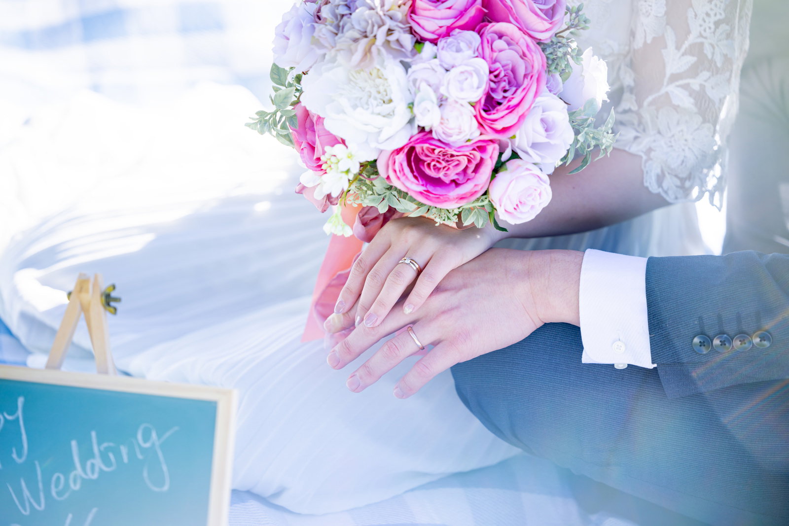 ピンクと白のブーケを手にした新婚夫婦が結婚指を付けた手を重ねている［モデル：河村友歌］