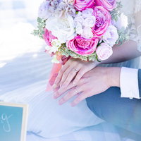 ピンクのブーケを持つふたりが結婚指を付けた手を重ねるの写真
