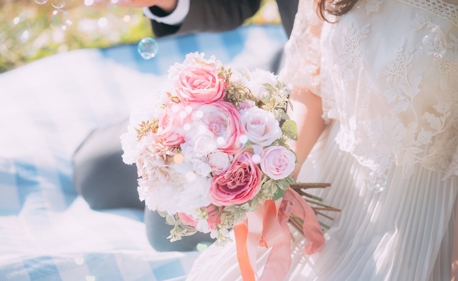 白いウェディングドレスを着た花嫁がピンク色のバラのブーケを持ち、シャボン玉が浮かんでいる［モデル：河村友歌］