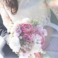 ピンク系ブーケを握るレース素材のドレス姿の女性の写真