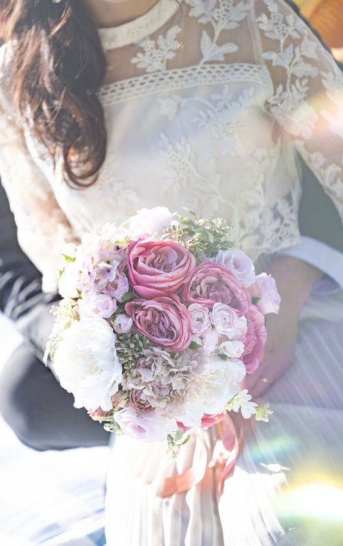 ピンク系ブーケを握るレース素材のドレス姿の女性