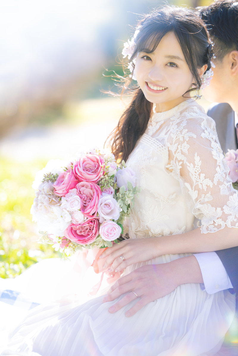 ピンクのブーケを持つウェディングドレス姿の花嫁が笑顔で横を向いている［モデル：河村友歌］
