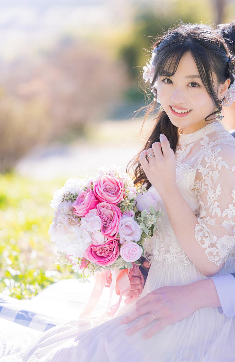 ウェディングドレス姿の新婦がピンクのバラのブーケを持って笑顔で立っている［モデル：河村友歌］
