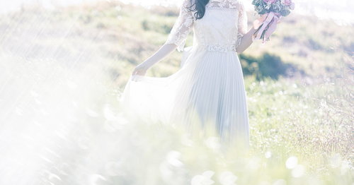 光が降り注ぐ野原でブーケを持つ花嫁の後ろ姿