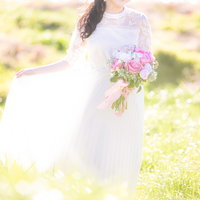 緑の野原で白いドレス姿の花嫁がピンクのブーケを手に微笑むの写真