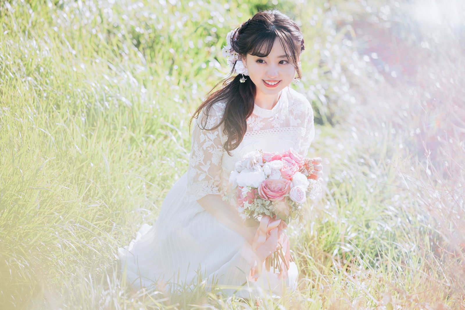 白いレースドレスの花嫁がピンク色のブーケを持って笑顔で立つ［モデル：河村友歌］