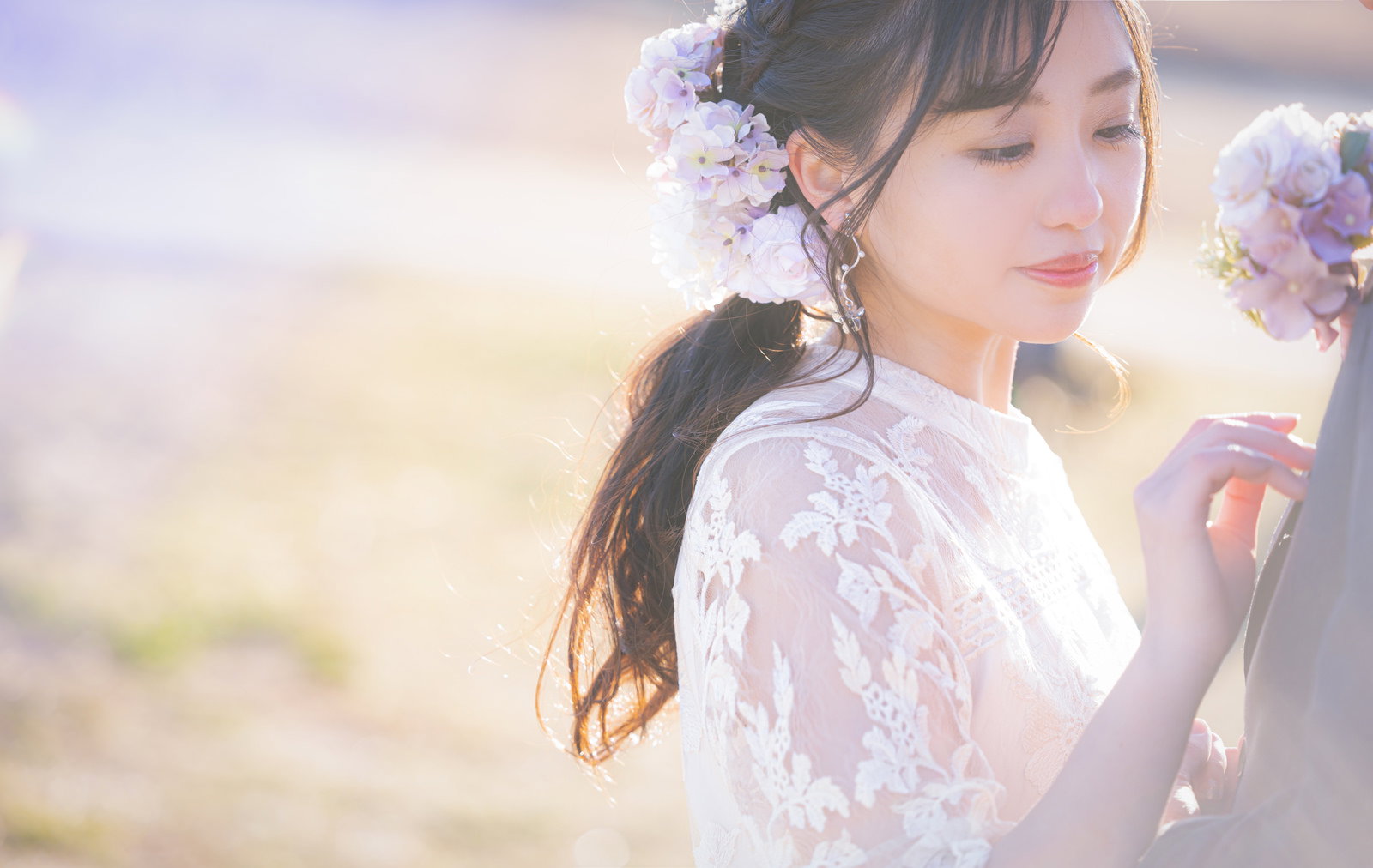 薄紫のアジサイを髪に飾り、白いレースのドレスを着た花嫁が下を向いている［モデル：河村友歌］