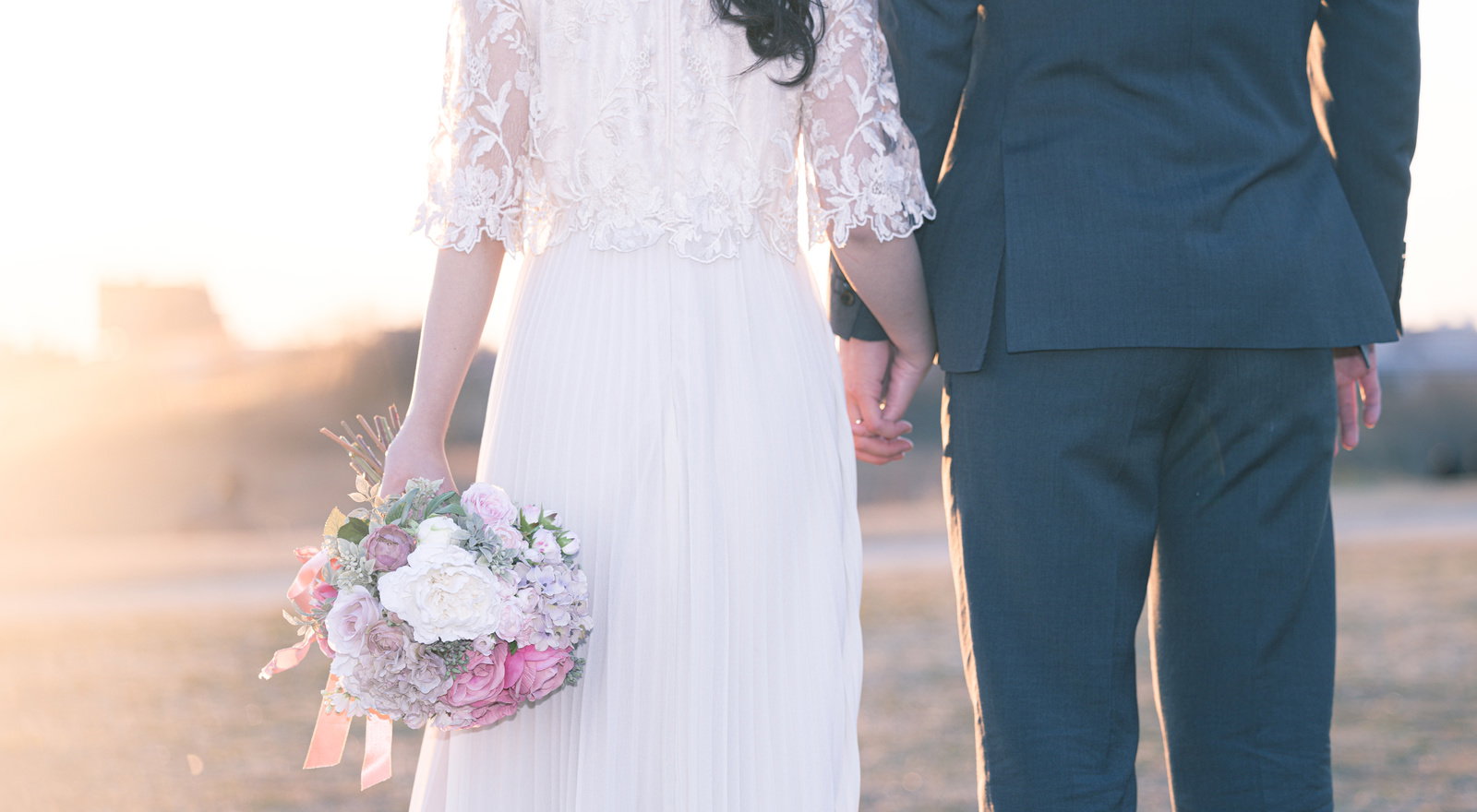 白いウェディングドレスと紺色のスーツを着た新婚夫婦が手を握り歩いている［モデル：河村友歌］