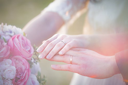 ピンクのブーケと結婚指輪を握る新婦の手の写真