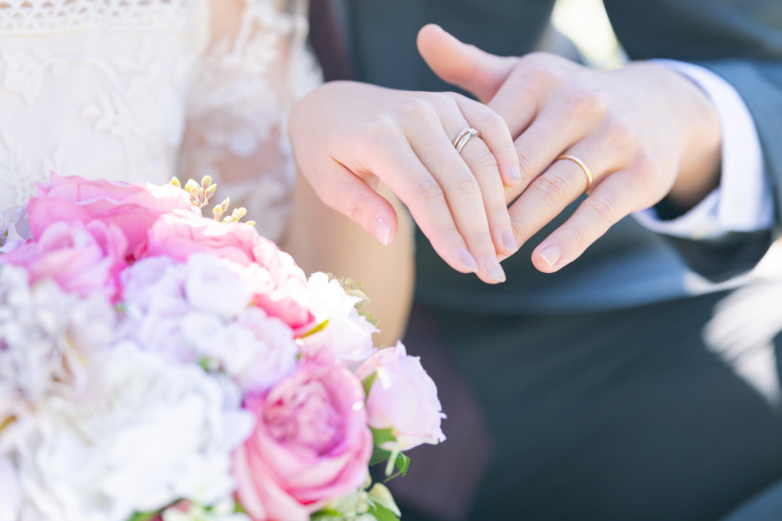 ピンク色のブーケの横で結婚指輪をした新郎新婦の手を重ねている［モデル：河村友歌］