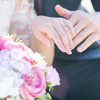 ふたりの結婚指輪とピンクのブーケ、新郎新婦の重ねた手の写真