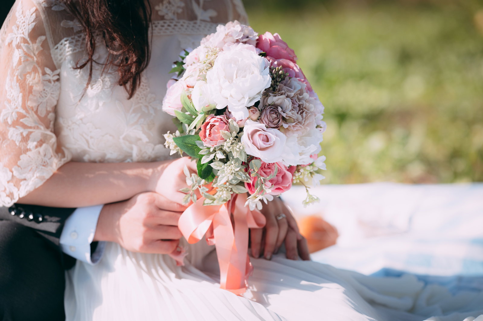 ピンクのリボン付きブーケを持つ花嫁と新郎が一緒にいる結婚式の場面［モデル：河村友歌］