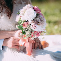 ピンクのリボンが付いたブーケを持つ花嫁と新郎の腕の写真