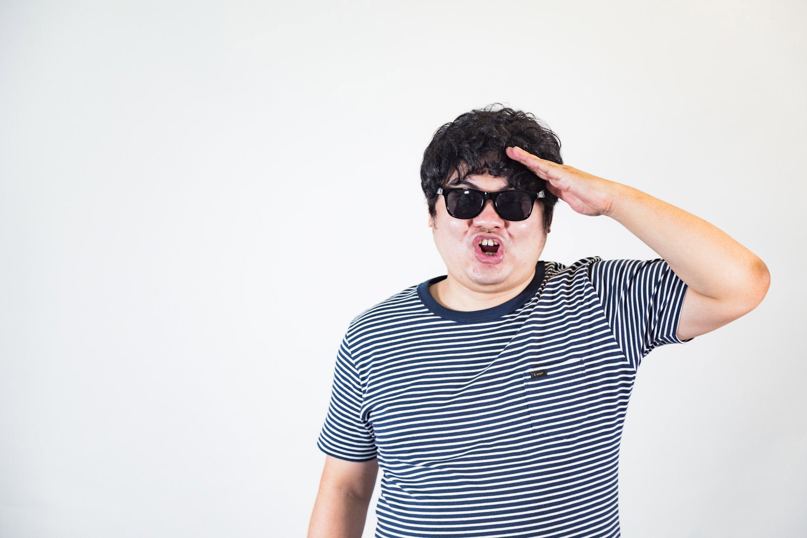 サングラスをかけた男性がボーダーTシャツ姿で片手を額に当てて敬礼している［モデル：段田隼人］