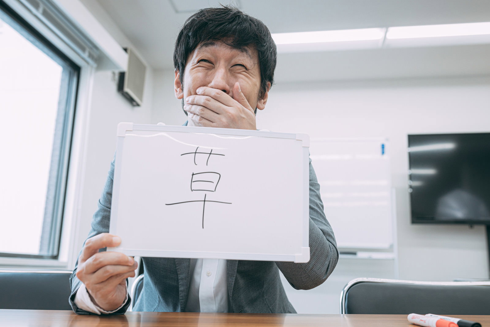 草ボードを持ち笑いを堪える男性［モデル：大川竜弥］