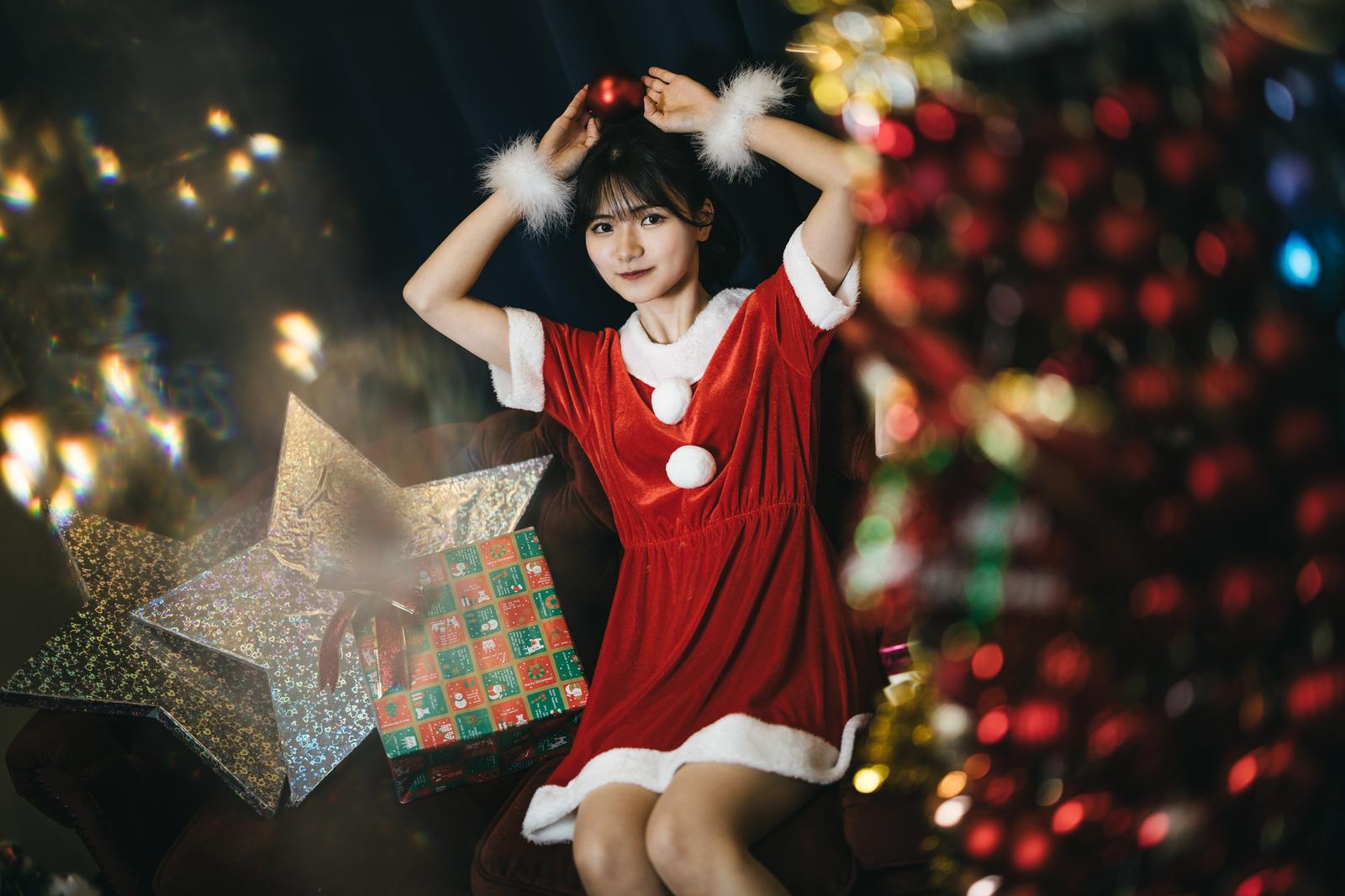 赤いサンタコスチュームを着た女性がクリスマスプレゼントを両手に持っている［モデル：モデルリリース］