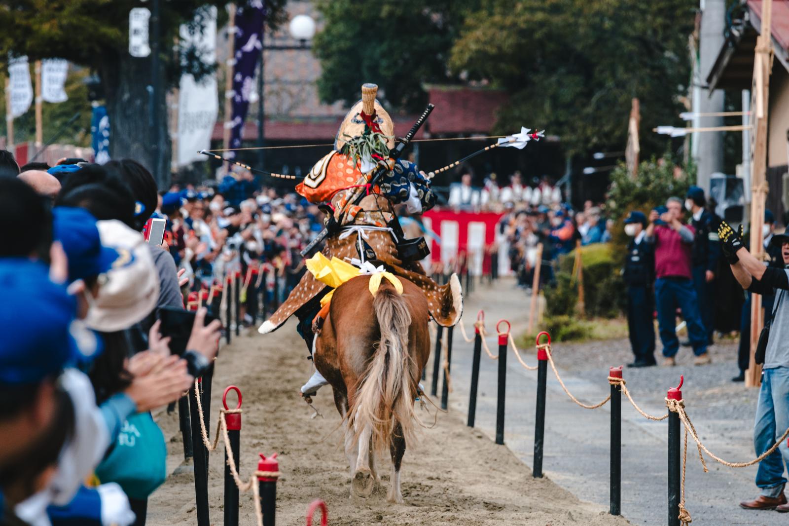 古殿八幡神社の流鏑馬で、馬上の射手がオレンジ色の衣装で矢を構えて疾走する
