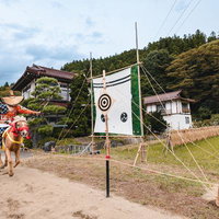 全速力で駆け抜ける馬の上から放たれた矢が的に向かう流鏑馬の写真