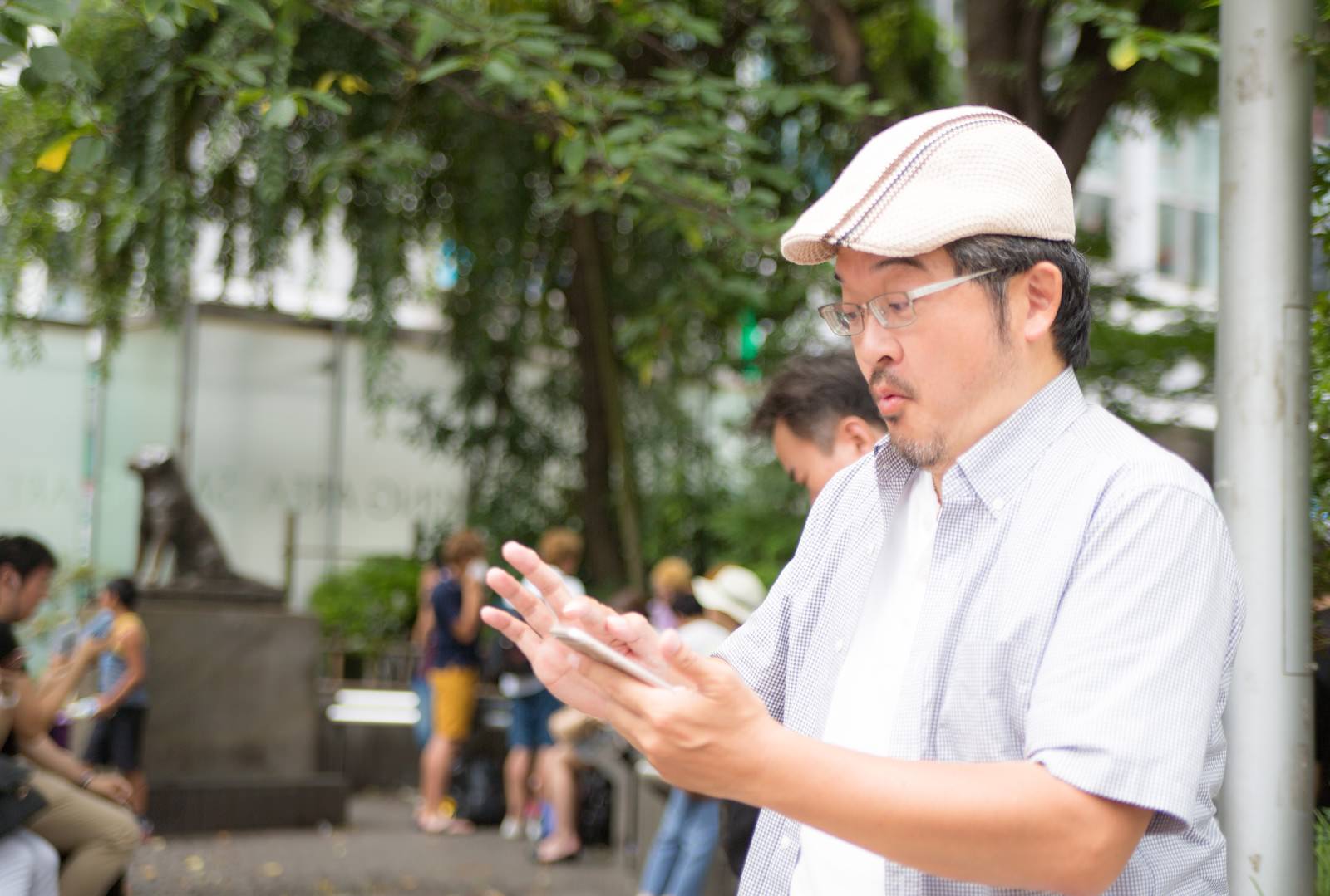 白赤チェック柄ハンチング帽の男性がスマートフォンを持ち両手を広げて喜んでいる［モデル：ナリシゲ］