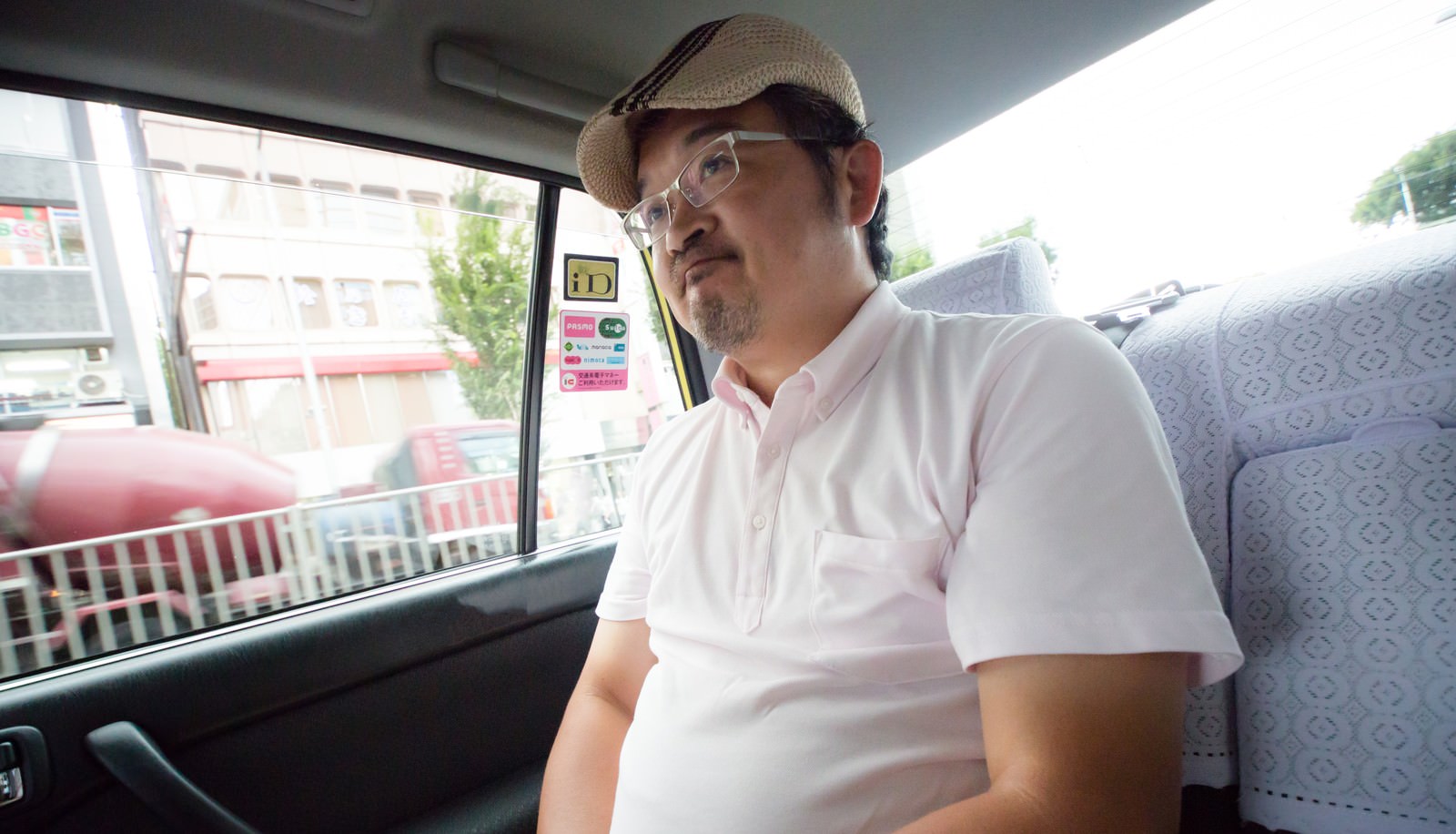 タクシー後部座席で苦笑いするハンチング帽の男性［モデル：ナリシゲ］