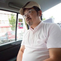 タクシーの車内で丸くなったと言われて苦笑いするハンチング帽の男性の写真