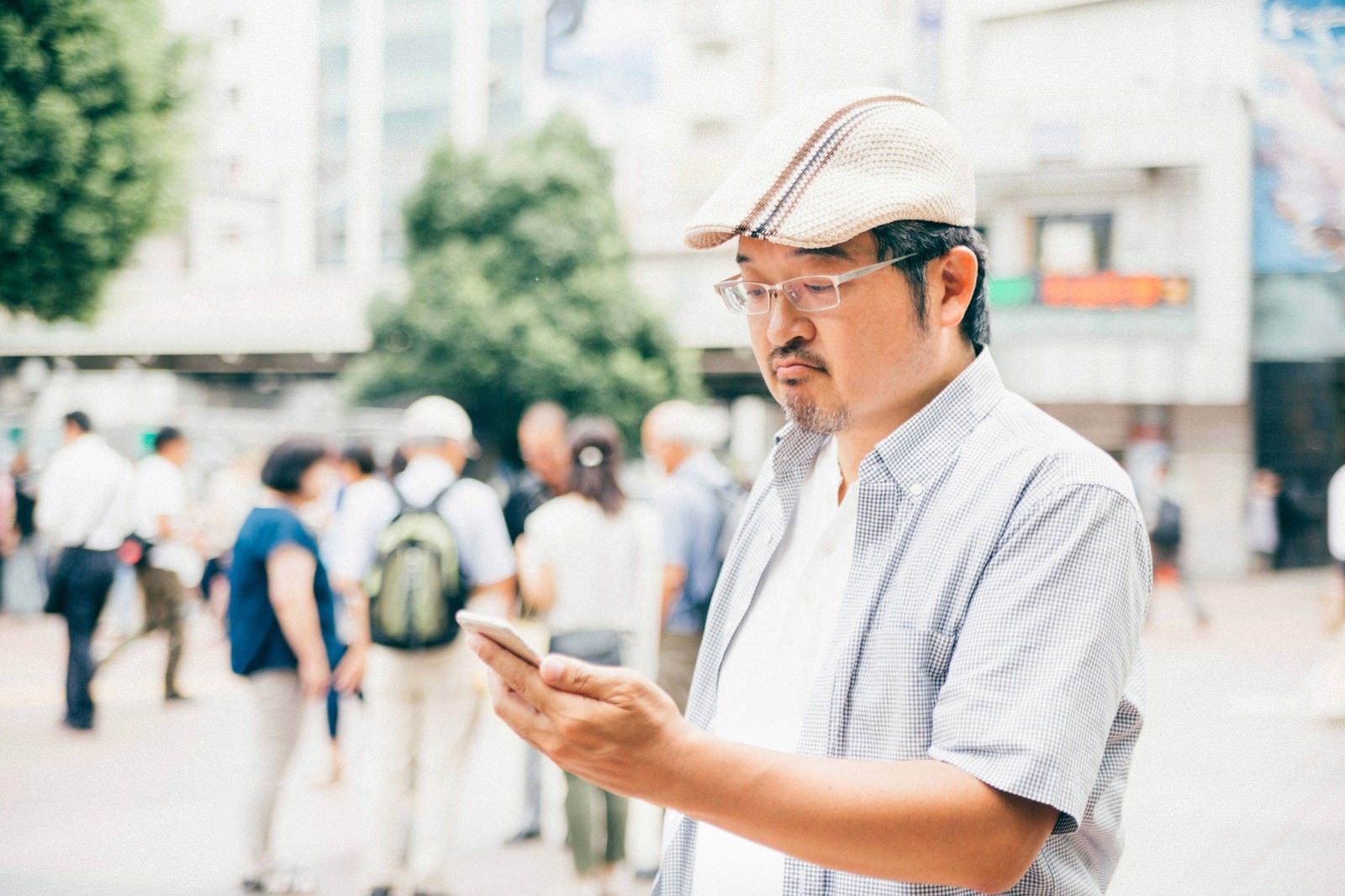 街中でスマートフォンを操作するハンチング帽の男性［モデル：ナリシゲ］