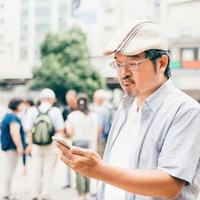 スマートフォンを見つめるハンチング帽の男性トレーナーの写真