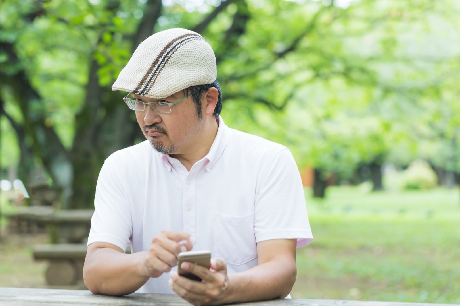 眉間にしわを寄せてスマホを操作するハンチング帽の男性［モデル：ナリシゲ］