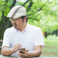 眉間にしわを寄せてスマホを操作するハンチング帽姿のコメンテーターの写真