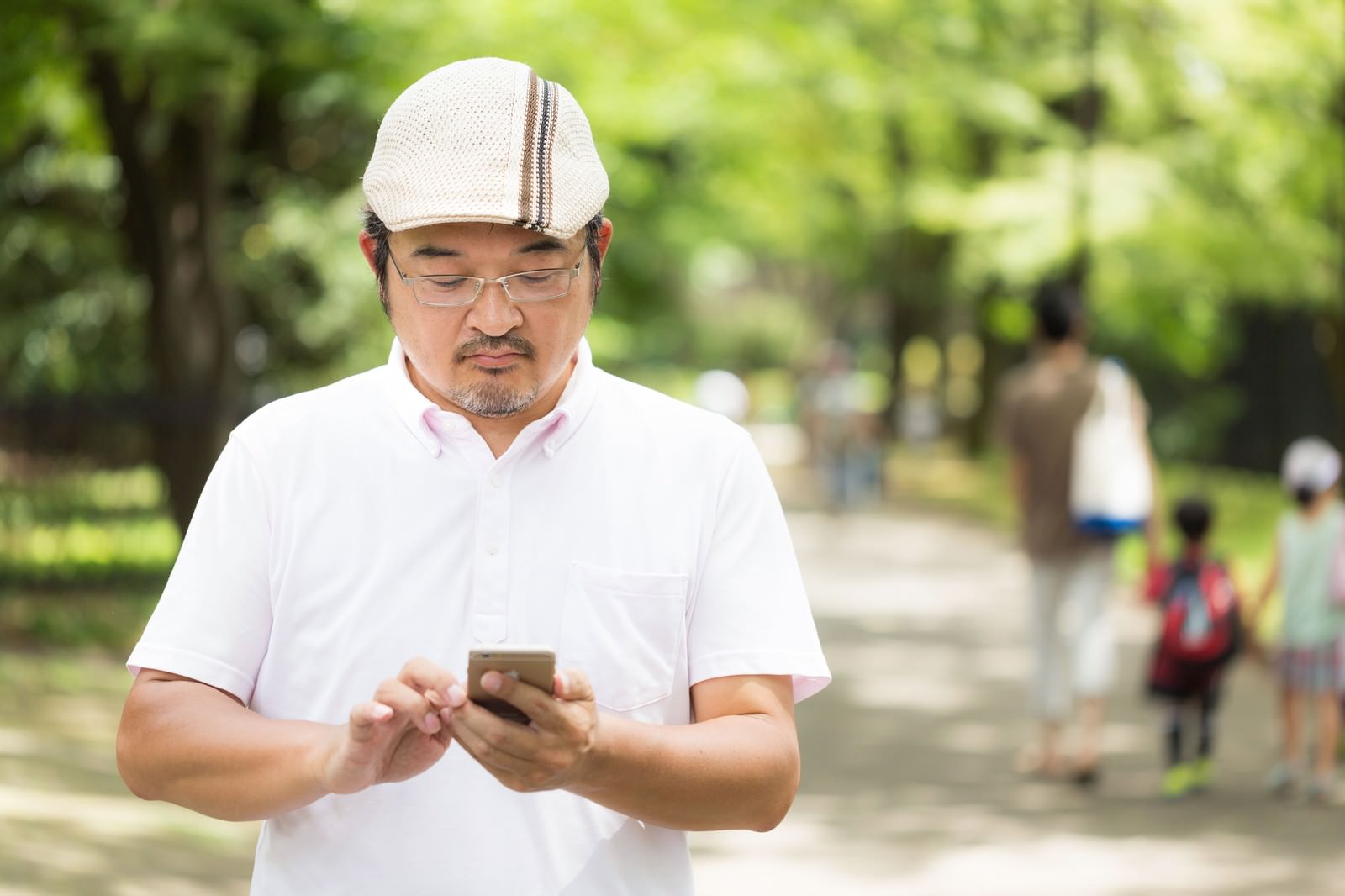 公園で歩きながらスマートフォンを操作するハンチング帽の男性［モデル：ナリシゲ］
