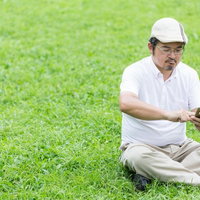 座り込み、ゲームに熱中してしまうハンチング帽の男性の写真
