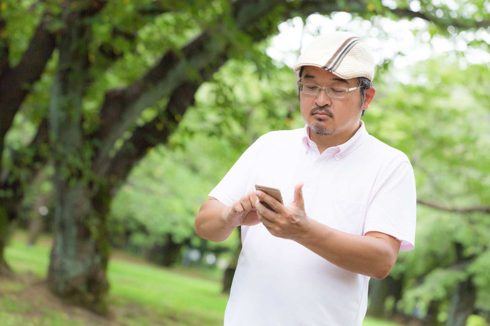 スマホを見ながら公園を歩く眼鏡の男性［モデル：ナリシゲ］